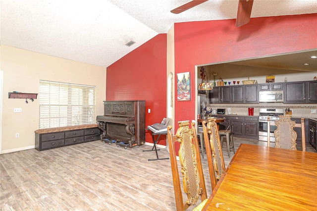 dining space featuring a textured ceiling, light hardwood / wood-style flooring, vaulted ceiling, and ceiling fan