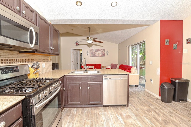 kitchen with kitchen peninsula, appliances with stainless steel finishes, backsplash, vaulted ceiling, and sink