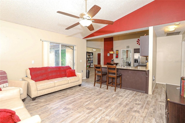 living room featuring sink, vaulted ceiling, ceiling fan, light wood-type flooring, and a textured ceiling