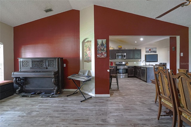 kitchen featuring appliances with stainless steel finishes, light hardwood / wood-style floors, lofted ceiling, and sink