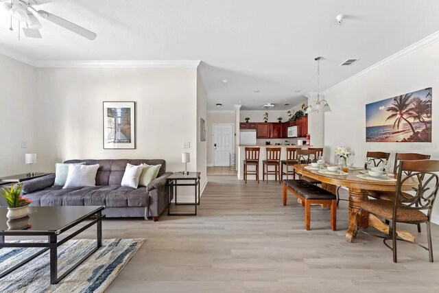 living room featuring ceiling fan with notable chandelier, light hardwood / wood-style flooring, and ornamental molding