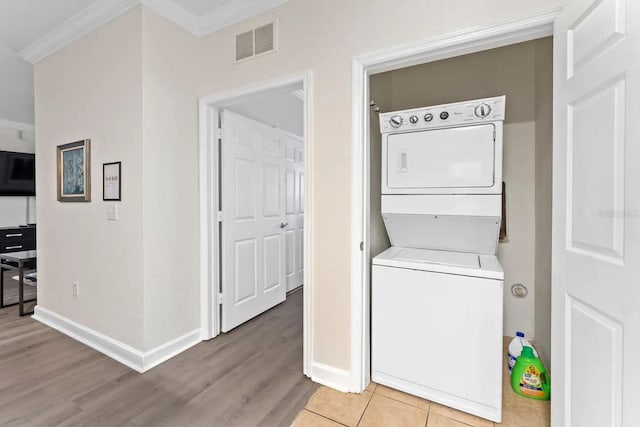 washroom featuring light wood finished floors, baseboards, visible vents, stacked washing maching and dryer, and laundry area