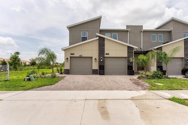 view of front of house with an attached garage, driveway, stone siding, and stucco siding