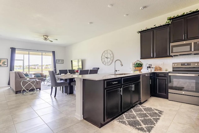 kitchen with light tile patterned flooring, sink, ceiling fan, stainless steel appliances, and kitchen peninsula