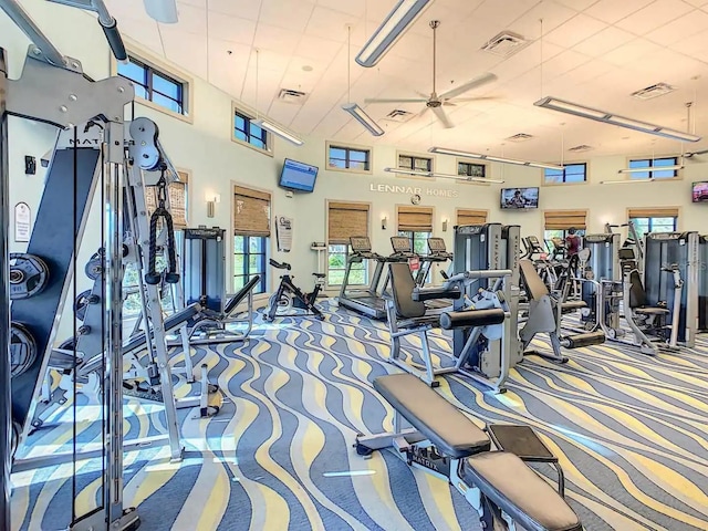 gym with ceiling fan, carpet, and a high ceiling