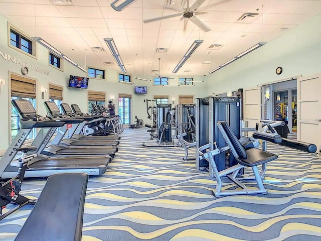 gym featuring ceiling fan, carpet flooring, and a high ceiling