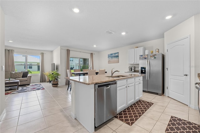 kitchen featuring a center island with sink, appliances with stainless steel finishes, light tile patterned flooring, a sink, and white cabinetry