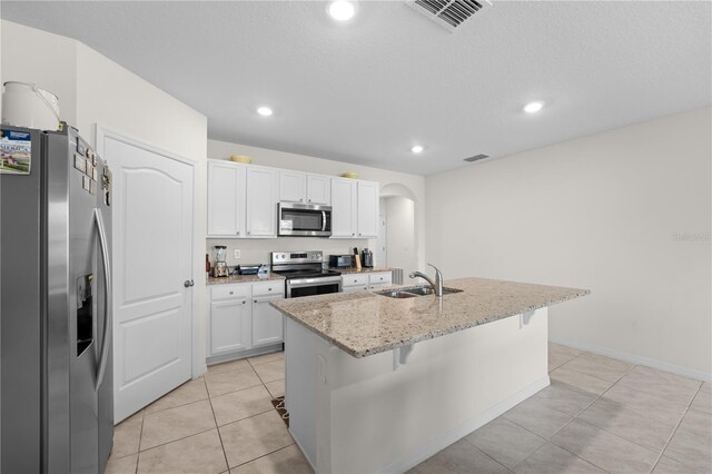 kitchen featuring a kitchen island with sink, appliances with stainless steel finishes, light stone countertops, light tile patterned floors, and sink