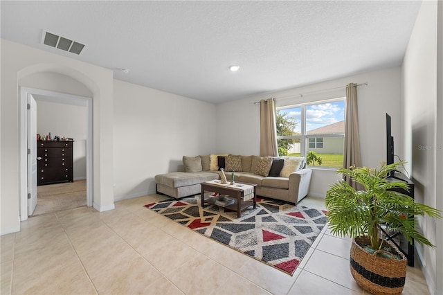 living room featuring light tile patterned floors, a textured ceiling, visible vents, and baseboards