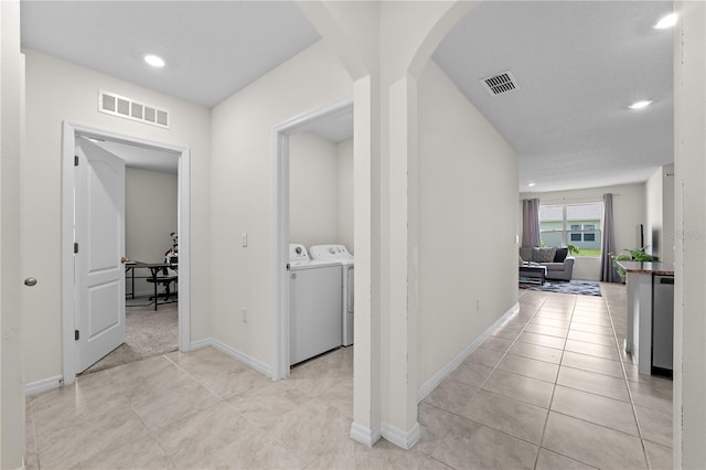 hallway with light tile patterned floors, visible vents, arched walkways, and washer and dryer