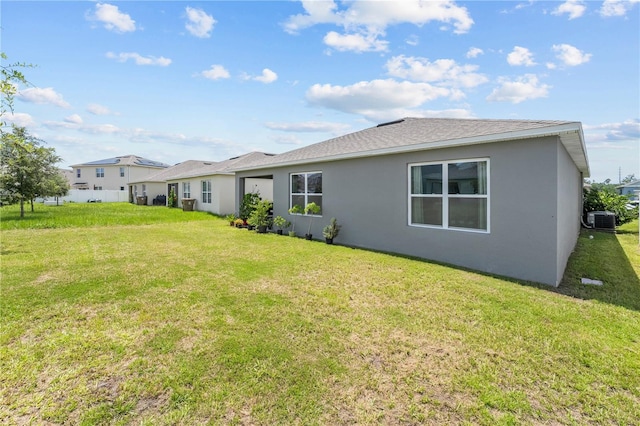 rear view of house with roof with shingles, stucco siding, a lawn, and central AC unit