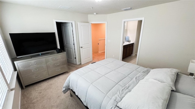 bedroom featuring light colored carpet, visible vents, a textured ceiling, and ensuite bathroom