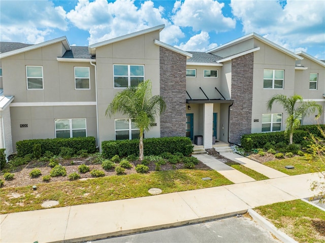 multi unit property featuring uncovered parking, stone siding, roof with shingles, and stucco siding