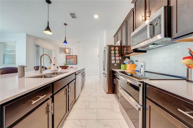 kitchen with stainless steel appliances, dark brown cabinets, light countertops, pendant lighting, and a sink