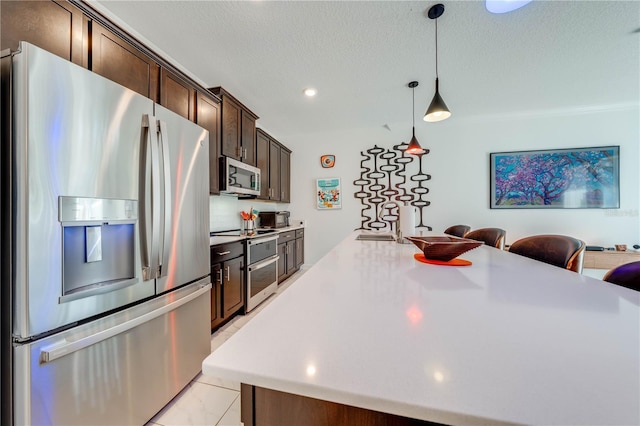 kitchen with dark brown cabinetry, appliances with stainless steel finishes, a breakfast bar, light countertops, and pendant lighting