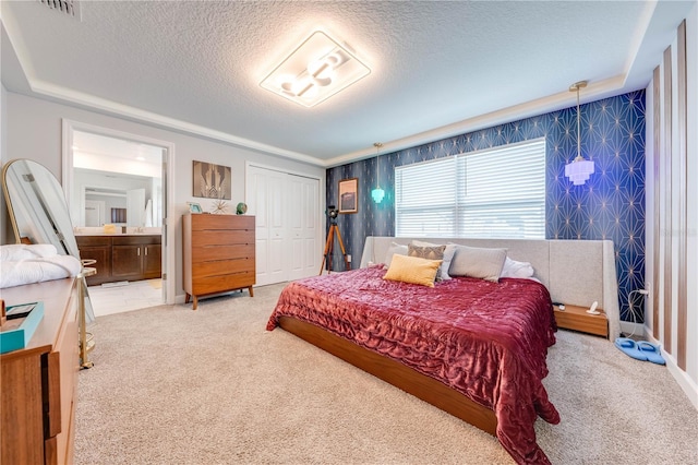 carpeted bedroom with a textured ceiling, a closet, visible vents, and ensuite bathroom