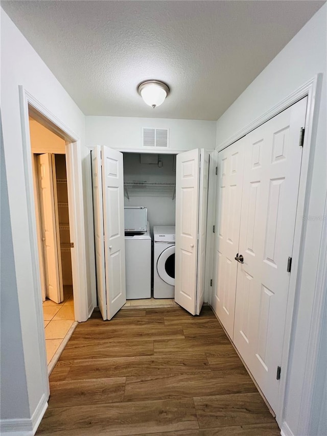 washroom with a textured ceiling, separate washer and dryer, and wood-type flooring