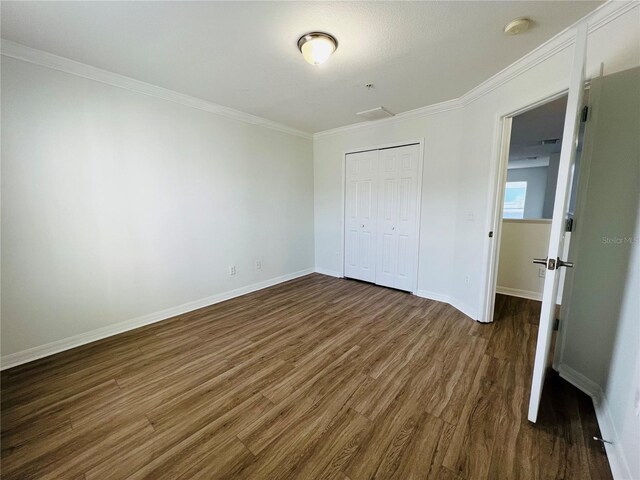 unfurnished bedroom with a closet, dark wood-type flooring, and ornamental molding