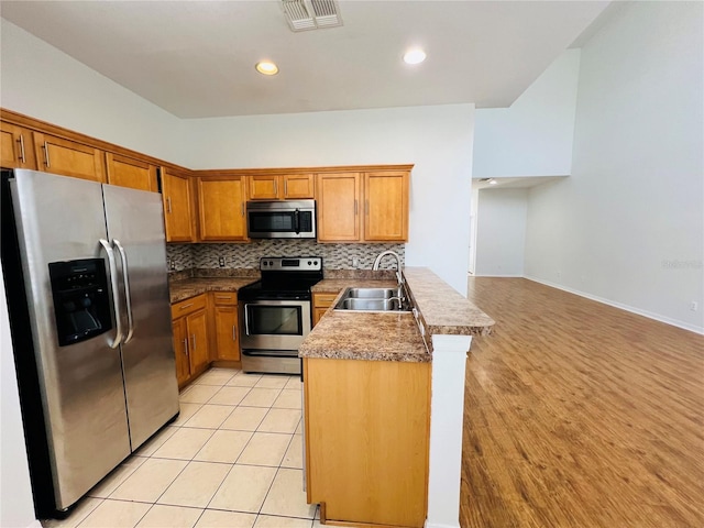 kitchen featuring sink, light hardwood / wood-style flooring, decorative backsplash, stainless steel appliances, and kitchen peninsula