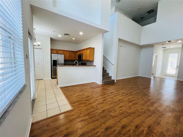 kitchen with a high ceiling, stainless steel appliances, light wood-type flooring, and tasteful backsplash