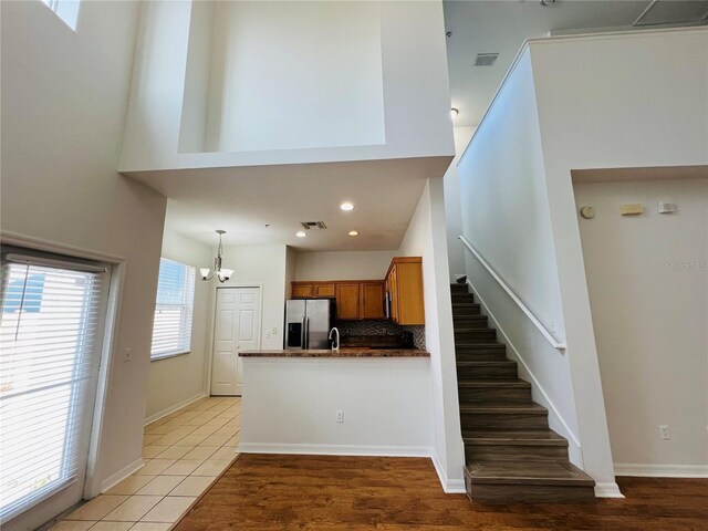 kitchen with backsplash, a towering ceiling, tile patterned flooring, stainless steel fridge with ice dispenser, and plenty of natural light