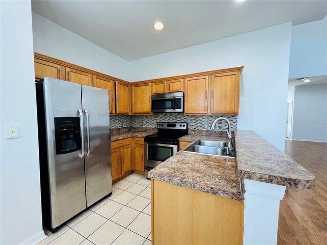 kitchen with decorative backsplash, appliances with stainless steel finishes, light hardwood / wood-style floors, sink, and kitchen peninsula