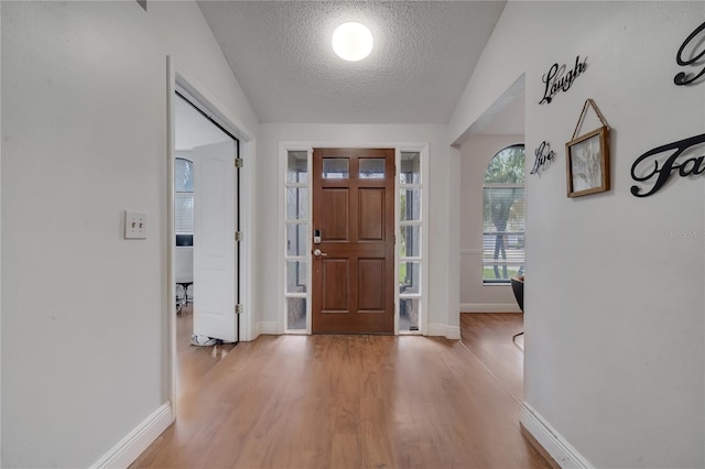 entrance foyer with light hardwood / wood-style flooring, vaulted ceiling, and a textured ceiling