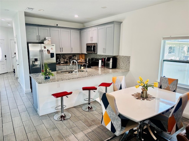 kitchen with stainless steel appliances, light stone counters, decorative backsplash, sink, and kitchen peninsula