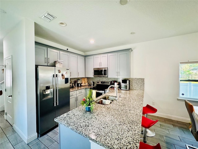 kitchen featuring gray cabinetry, a kitchen breakfast bar, stainless steel appliances, light stone counters, and backsplash