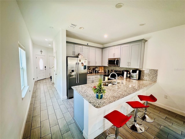 kitchen with stainless steel appliances, kitchen peninsula, light stone countertops, a breakfast bar area, and tasteful backsplash