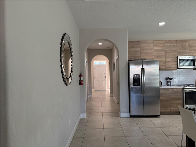 kitchen featuring a textured ceiling, decorative backsplash, light tile patterned floors, and stainless steel appliances