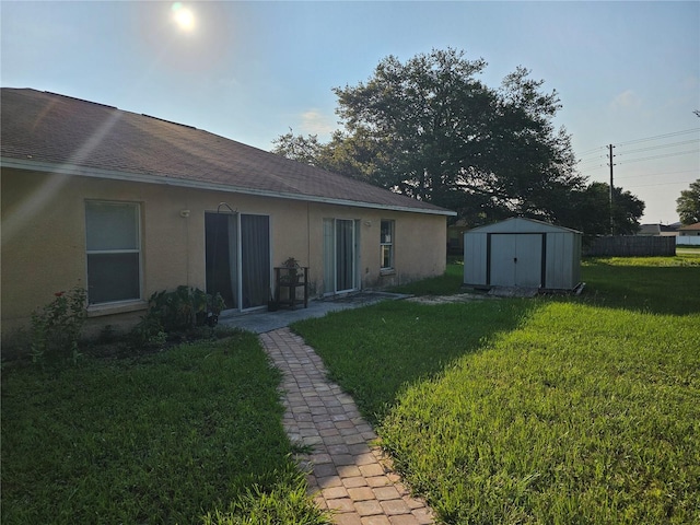 back of property featuring an outbuilding, stucco siding, a shingled roof, a storage unit, and a lawn