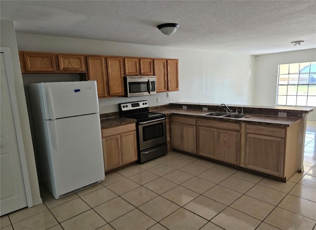 kitchen featuring dark countertops, a peninsula, stainless steel appliances, and a sink