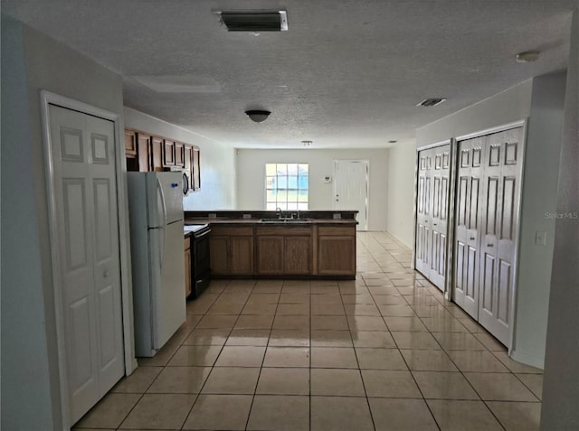 kitchen with sink, a textured ceiling, light tile patterned floors, kitchen peninsula, and white refrigerator