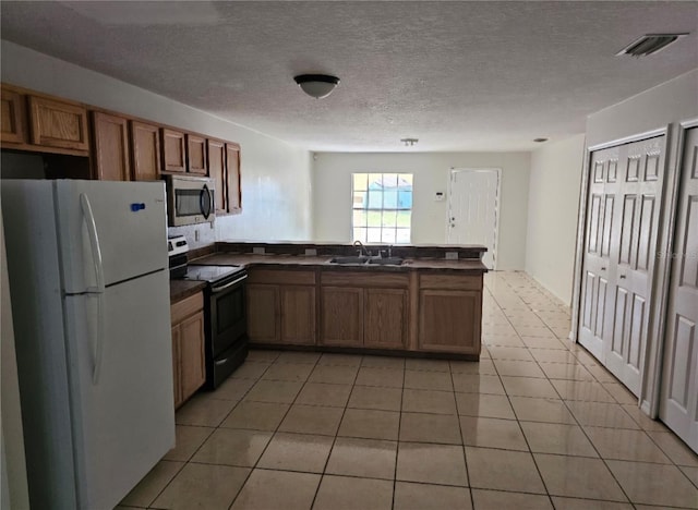 kitchen with range with electric cooktop, dark countertops, stainless steel microwave, freestanding refrigerator, and a peninsula