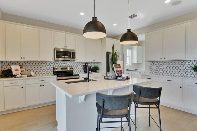 kitchen featuring appliances with stainless steel finishes, light wood-type flooring, decorative light fixtures, and an island with sink