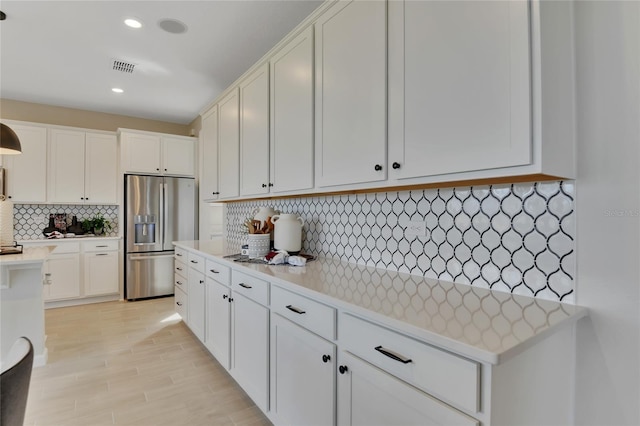 kitchen with white cabinets, stainless steel refrigerator with ice dispenser, light hardwood / wood-style floors, and decorative backsplash