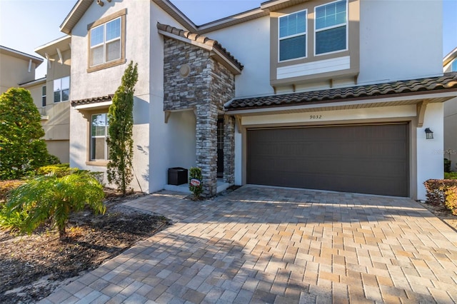 view of front of home featuring an attached garage, stucco siding, stone siding, a tile roof, and decorative driveway