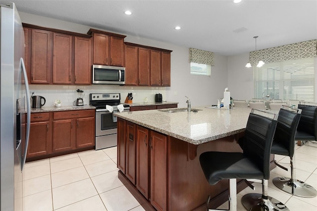 kitchen with light tile patterned flooring, a sink, stainless steel appliances, a kitchen breakfast bar, and backsplash