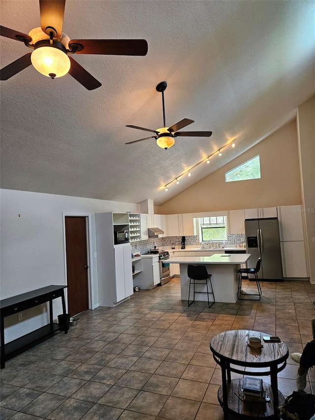 interior space with white cabinets, vaulted ceiling, appliances with stainless steel finishes, dark tile patterned flooring, and a center island