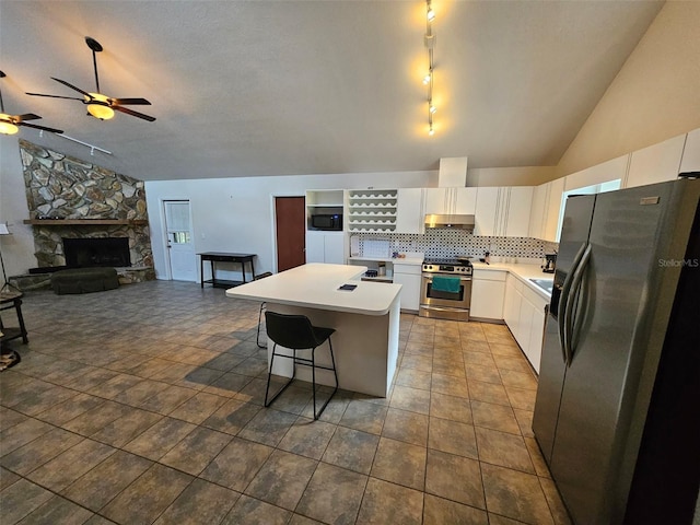 kitchen with appliances with stainless steel finishes, white cabinetry, dark tile patterned flooring, ceiling fan, and a stone fireplace