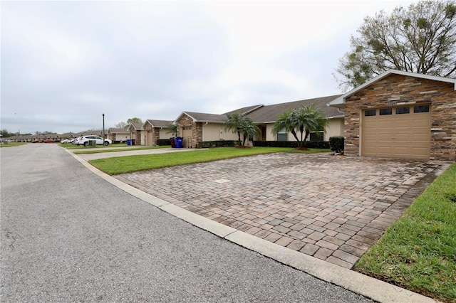 ranch-style house featuring a front yard, stucco siding, a garage, stone siding, and decorative driveway