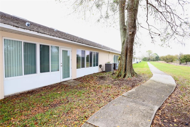 view of side of home with central air condition unit, a yard, and stucco siding