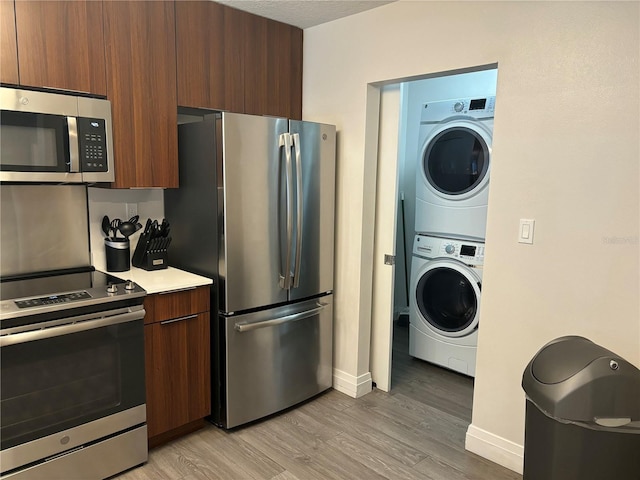 kitchen with light countertops, appliances with stainless steel finishes, light wood-type flooring, stacked washing maching and dryer, and modern cabinets