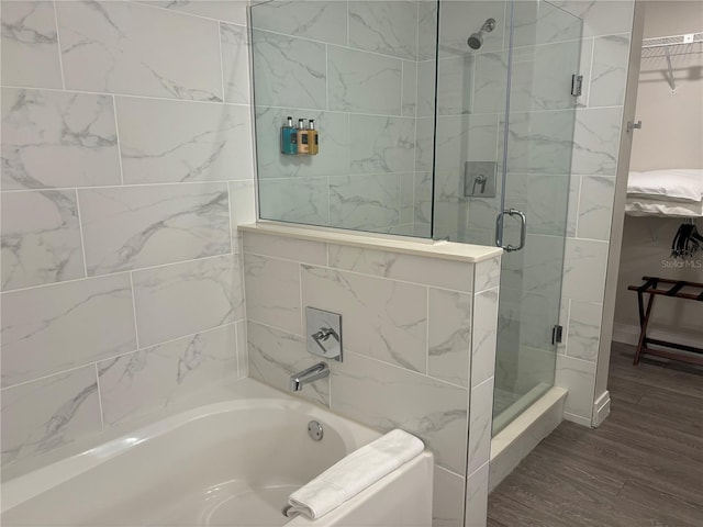 full bath with a spacious closet, a stall shower, wood finished floors, and a bath