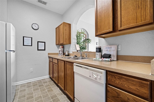 kitchen with sink, light tile patterned floors, white dishwasher, and stainless steel refrigerator