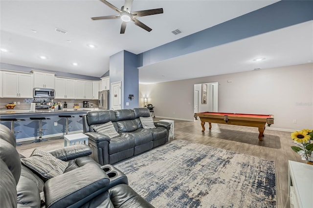 living area featuring visible vents, baseboards, light wood-style floors, and vaulted ceiling