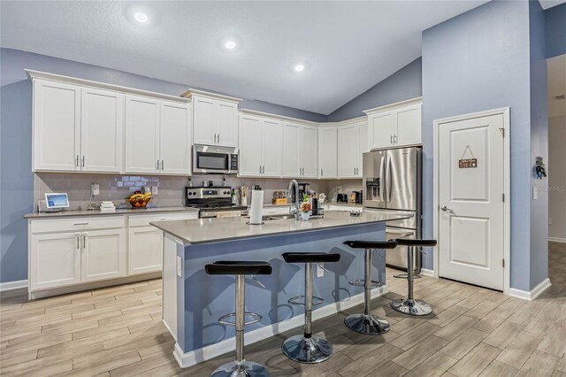 kitchen with light hardwood / wood-style flooring, a kitchen bar, stainless steel appliances, vaulted ceiling, and a center island with sink