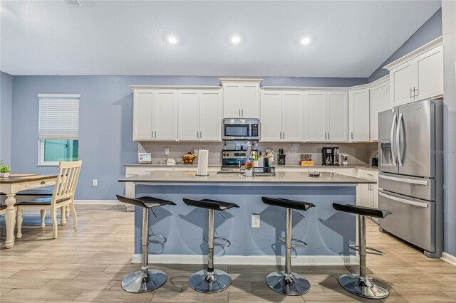 kitchen with light wood-type flooring, a kitchen bar, stainless steel appliances, an island with sink, and vaulted ceiling