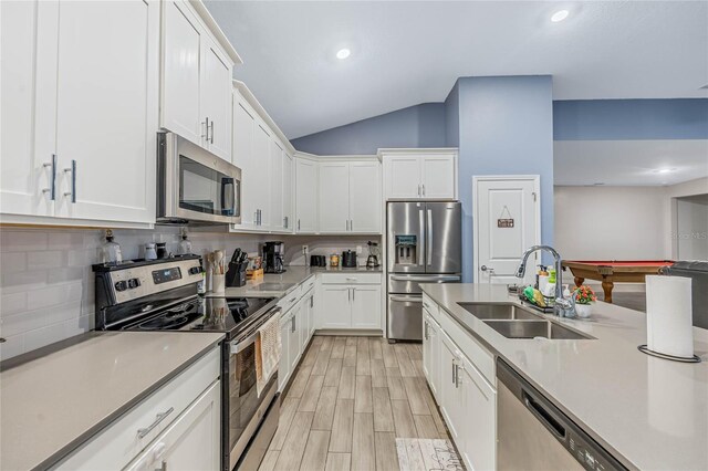 kitchen with lofted ceiling, stainless steel appliances, white cabinetry, and sink